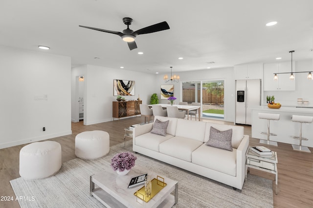 living room featuring ceiling fan with notable chandelier and light wood-type flooring