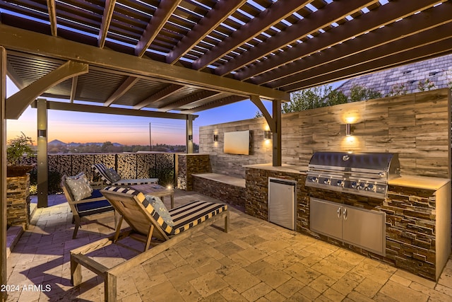 patio terrace at dusk with a pergola, an outdoor kitchen, and grilling area