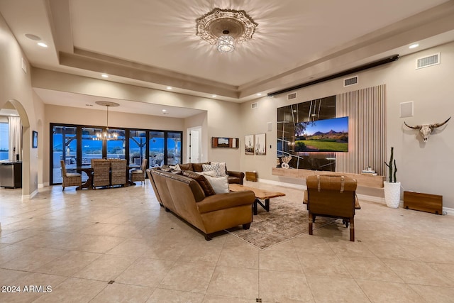 living room featuring light tile patterned floors, a tray ceiling, and an inviting chandelier