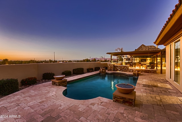 pool at dusk with a patio area and a fireplace