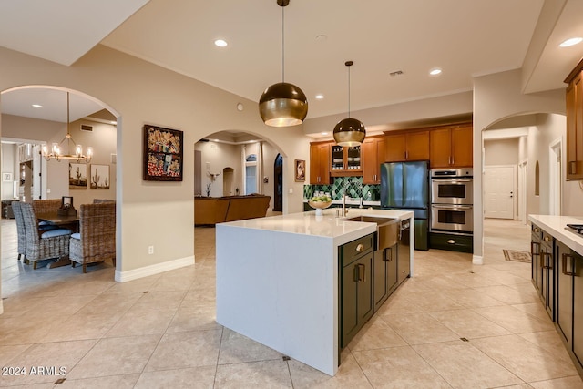 kitchen featuring stainless steel appliances, light tile patterned floors, a chandelier, hanging light fixtures, and an island with sink