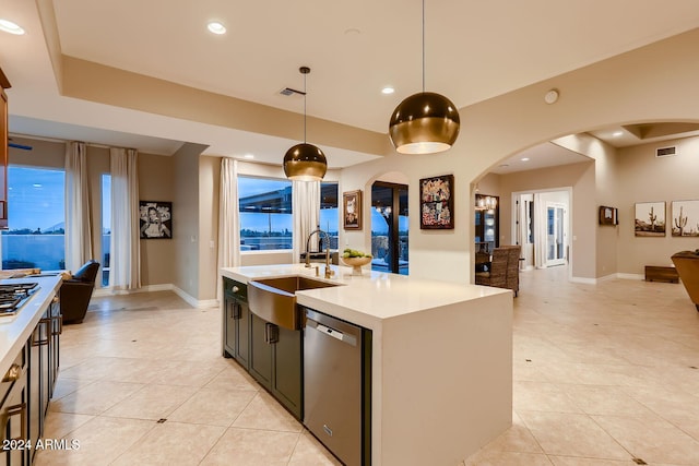 kitchen featuring appliances with stainless steel finishes, sink, light tile patterned floors, decorative light fixtures, and a center island with sink