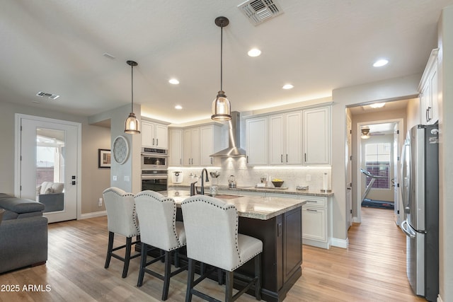 kitchen featuring stainless steel appliances, tasteful backsplash, light stone countertops, white cabinets, and wall chimney exhaust hood