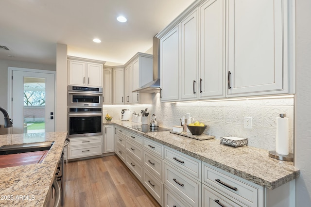 kitchen featuring double oven, sink, backsplash, light stone counters, and black electric cooktop