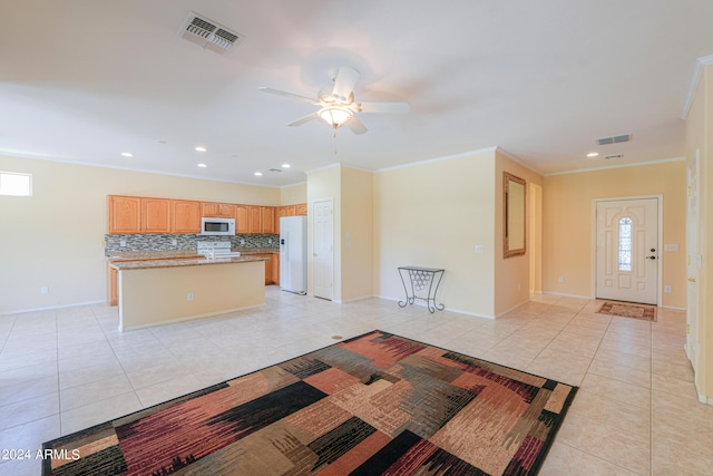 kitchen with white appliances, light tile patterned floors, visible vents, a kitchen island, and decorative backsplash