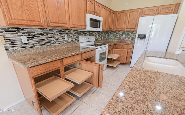 kitchen with light stone countertops, white appliances, light tile patterned floors, and a sink