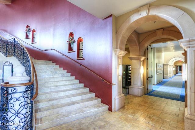 stairs featuring arched walkways, stone finish flooring, and decorative columns