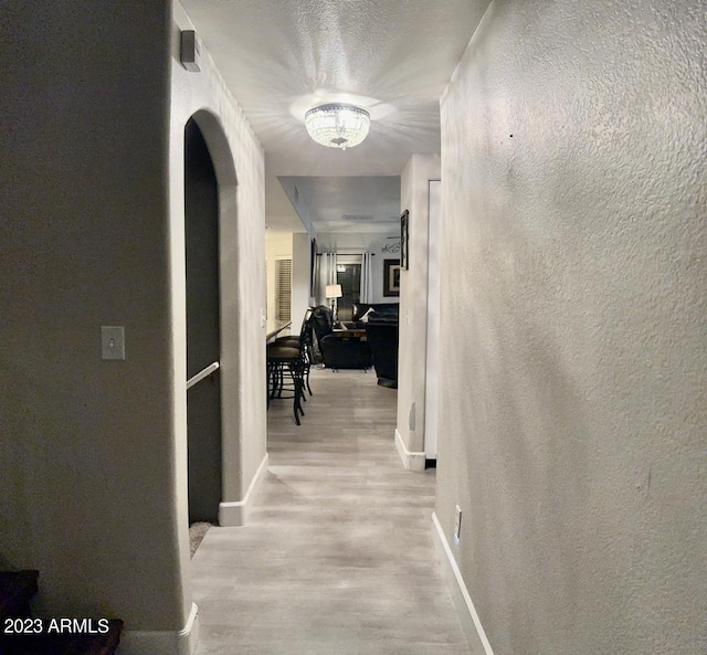 corridor with baseboards, a chandelier, a textured wall, wood finished floors, and arched walkways