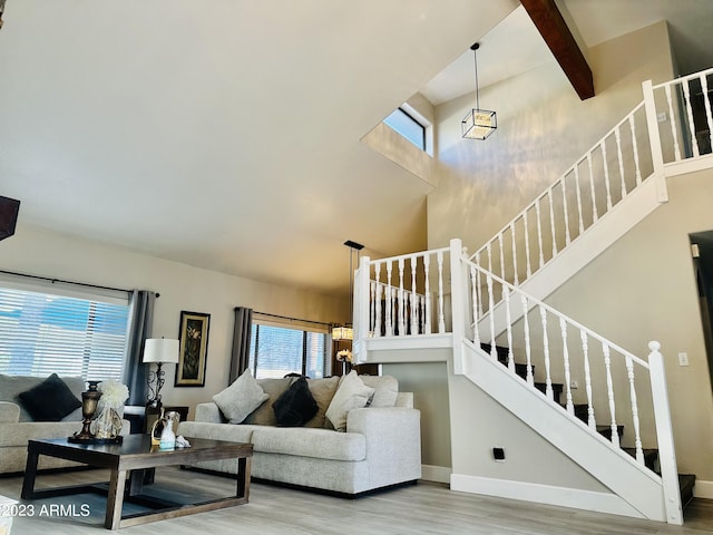 living room featuring beam ceiling, a high ceiling, wood finished floors, and stairs