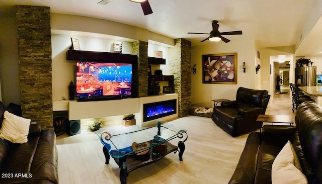 living area with wood finished floors, a warm lit fireplace, and ceiling fan