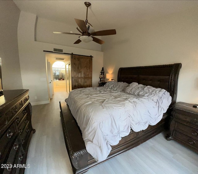 bedroom featuring visible vents, wood finished floors, a barn door, baseboards, and ceiling fan