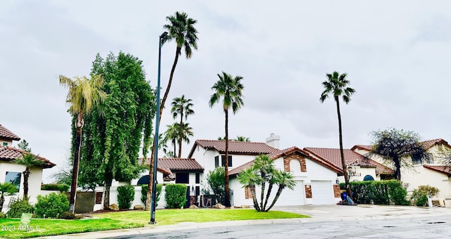 mediterranean / spanish home with a front lawn, a tiled roof, concrete driveway, stucco siding, and an attached garage