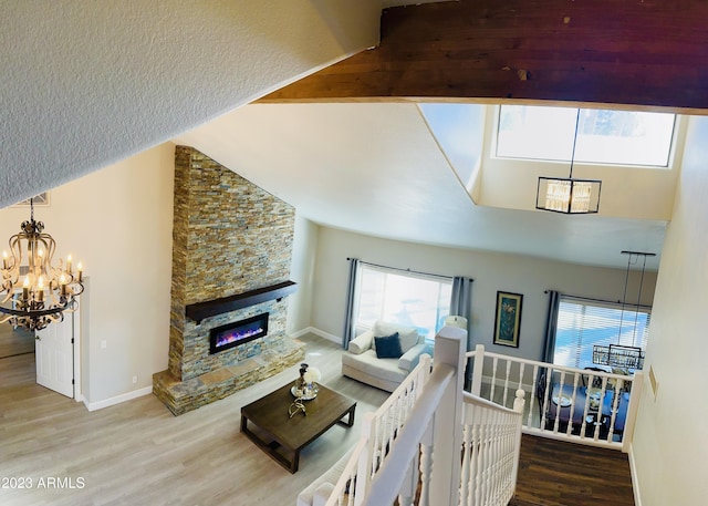 living room with high vaulted ceiling, wood finished floors, a stone fireplace, an inviting chandelier, and baseboards