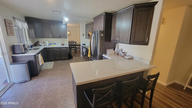 kitchen featuring a kitchen bar, sink, dark brown cabinets, stainless steel fridge, and kitchen peninsula