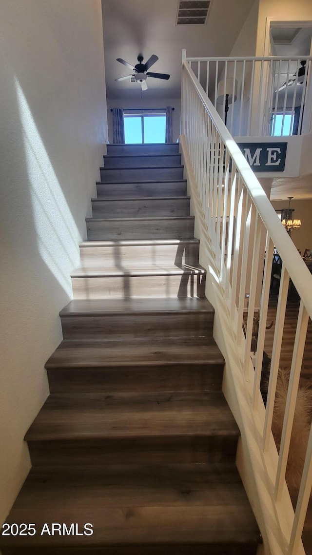 stairs featuring ceiling fan with notable chandelier