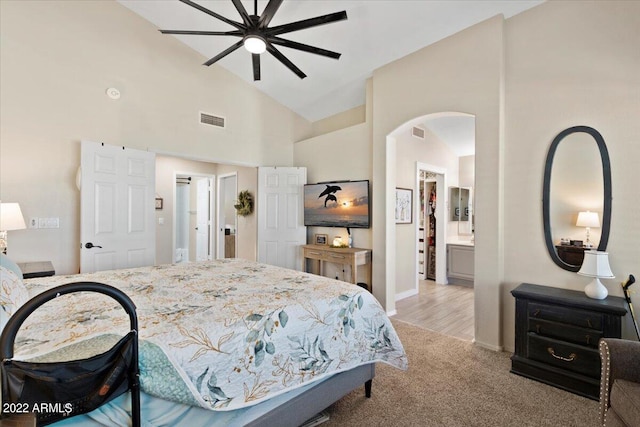 bedroom featuring light carpet, high vaulted ceiling, ceiling fan, and connected bathroom