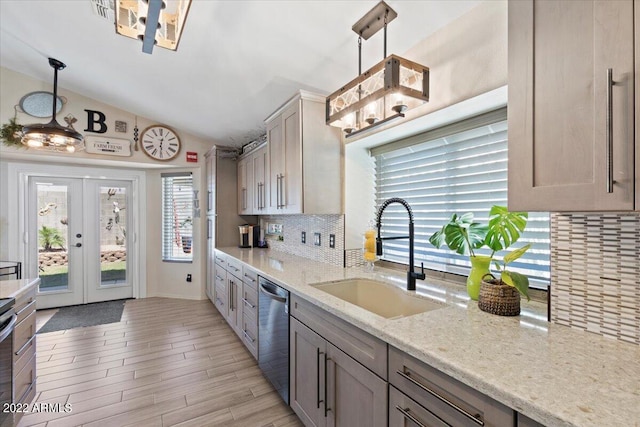 kitchen with lofted ceiling, light stone counters, stainless steel dishwasher, sink, and hanging light fixtures