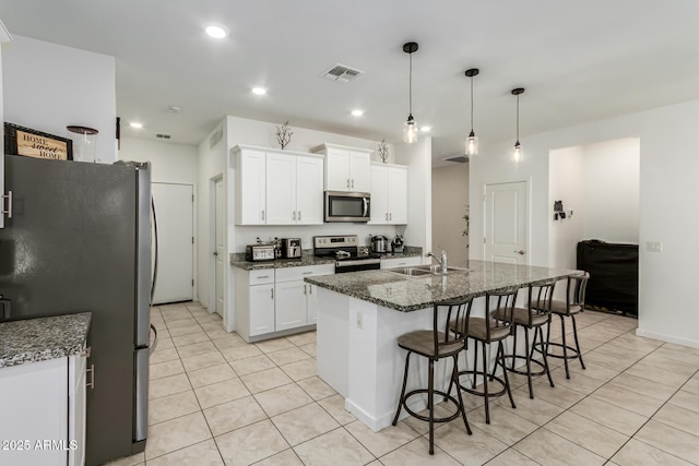 kitchen with a sink, stainless steel appliances, light tile patterned floors, a kitchen bar, and white cabinetry