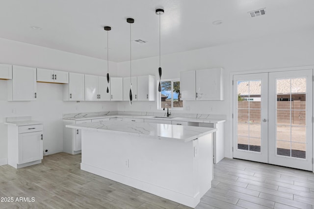 kitchen with a kitchen island, a sink, visible vents, white cabinetry, and french doors