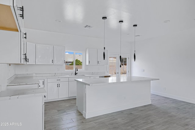 kitchen with a center island, pendant lighting, visible vents, light wood-style flooring, and white cabinets