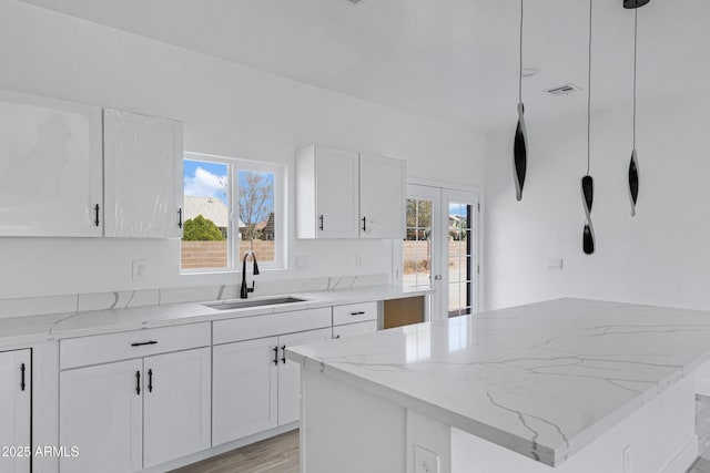 kitchen with light wood-style flooring, a sink, visible vents, white cabinets, and light stone countertops