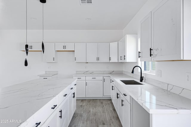 kitchen featuring light stone counters, a sink, visible vents, light wood-style floors, and white cabinets