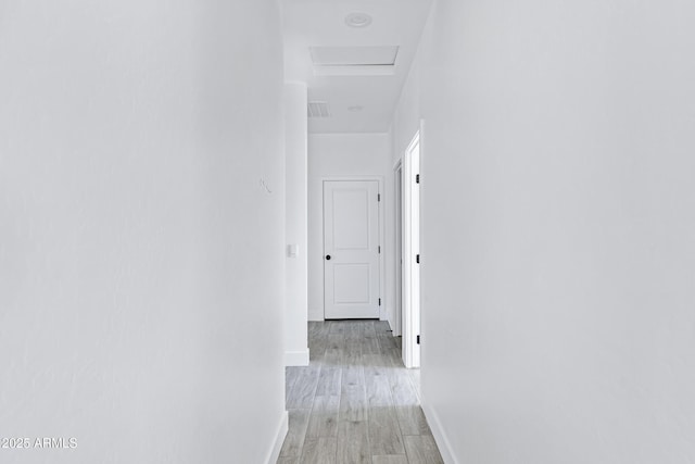 hallway featuring attic access, visible vents, light wood-style flooring, and baseboards