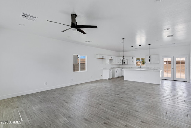 unfurnished living room featuring light wood-style floors, french doors, visible vents, and baseboards