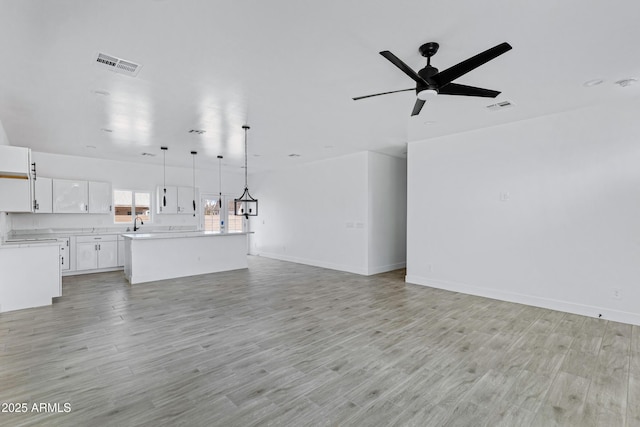 unfurnished living room with ceiling fan, light wood-type flooring, visible vents, and baseboards