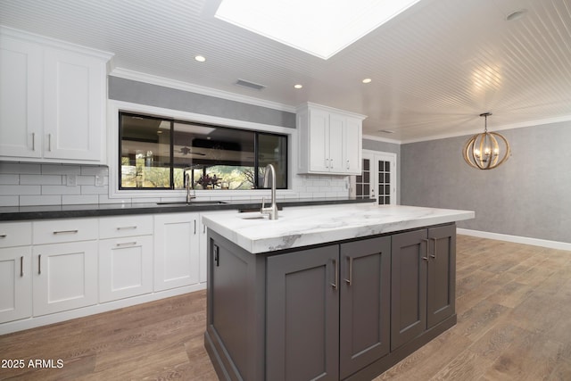 kitchen featuring a kitchen island with sink, a sink, visible vents, white cabinets, and dark stone countertops