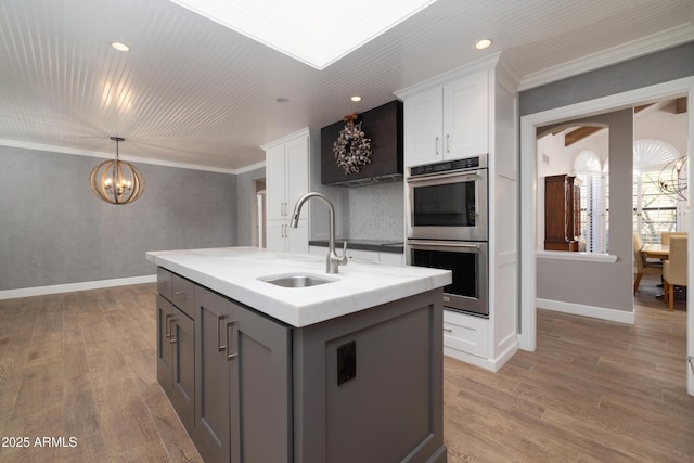 kitchen with an island with sink, double oven, white cabinetry, and a sink