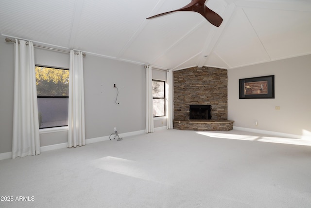 unfurnished living room with lofted ceiling with beams, ceiling fan, a stone fireplace, carpet floors, and baseboards