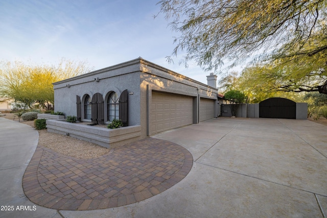 view of side of home featuring a garage, a gate, driveway, and stucco siding