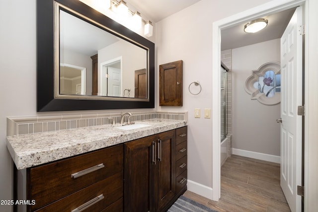 bathroom with bath / shower combo with glass door, wood finished floors, vanity, and baseboards