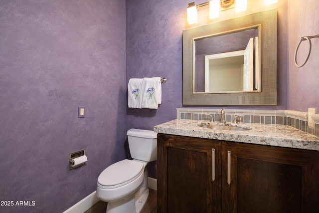 half bathroom featuring toilet, baseboards, and vanity