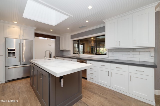 kitchen with a kitchen island with sink, stainless steel appliances, a skylight, and white cabinetry