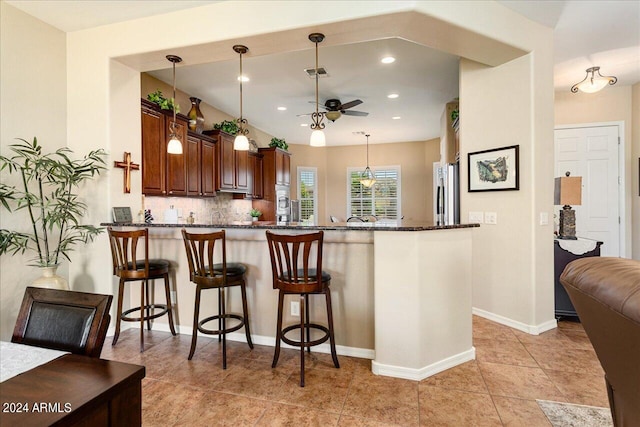 kitchen featuring ceiling fan, backsplash, hanging light fixtures, kitchen peninsula, and light tile patterned flooring