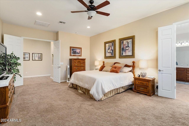 bedroom with ceiling fan, light colored carpet, and ensuite bath