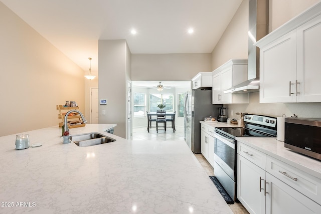 kitchen with wall chimney range hood, light stone counters, appliances with stainless steel finishes, white cabinets, and a sink