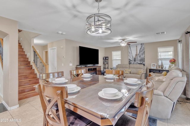 dining room featuring ceiling fan with notable chandelier, visible vents, stairway, and light tile patterned floors