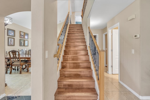 stairs with tile patterned floors, arched walkways, and baseboards