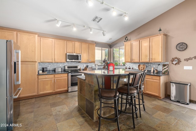 kitchen with light brown cabinets, tasteful backsplash, appliances with stainless steel finishes, and vaulted ceiling