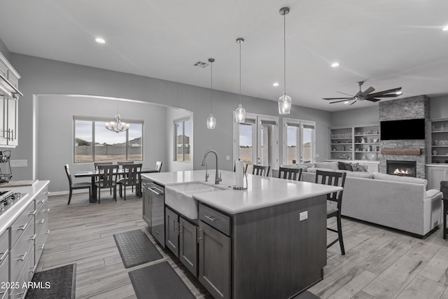 kitchen featuring a kitchen bar, light wood-type flooring, a sink, stainless steel dishwasher, and a stone fireplace