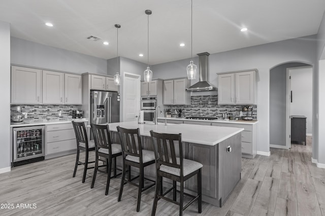 kitchen with beverage cooler, arched walkways, light countertops, appliances with stainless steel finishes, and wall chimney range hood