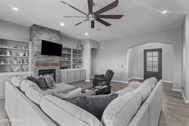 living area featuring a ceiling fan, light wood finished floors, recessed lighting, arched walkways, and a stone fireplace