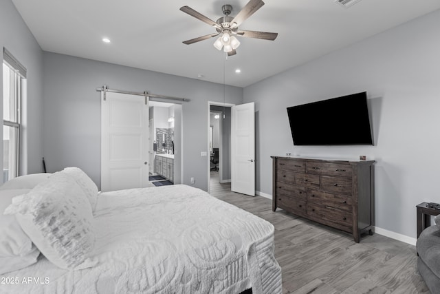 bedroom featuring connected bathroom, baseboards, a barn door, recessed lighting, and wood finished floors