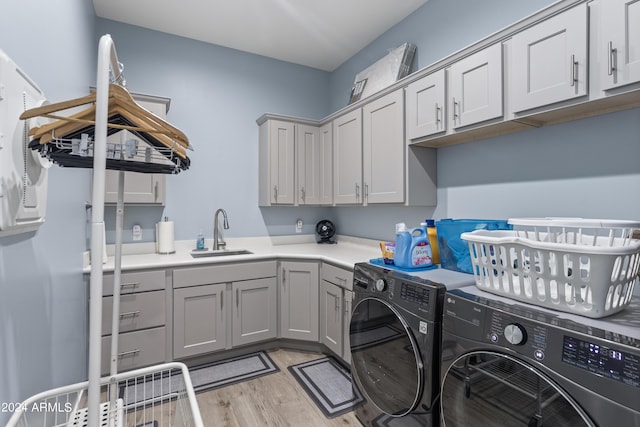 laundry room featuring washing machine and clothes dryer, light wood-style flooring, cabinet space, and a sink