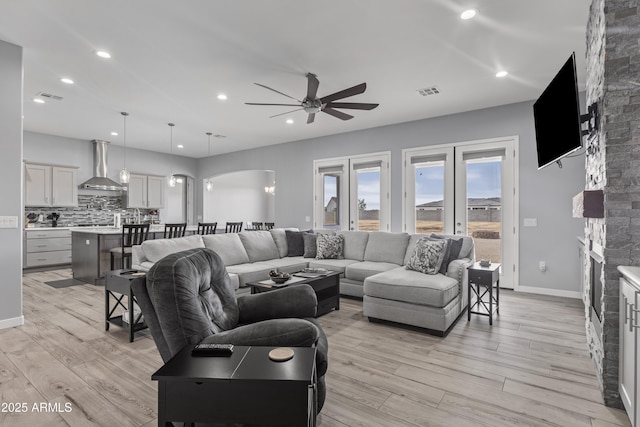 living area featuring visible vents, arched walkways, a fireplace, light wood finished floors, and ceiling fan