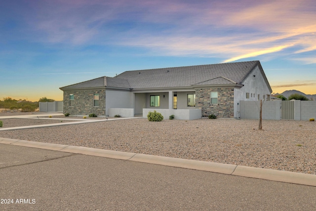 view of front of house with a gate, stone siding, stucco siding, and fence