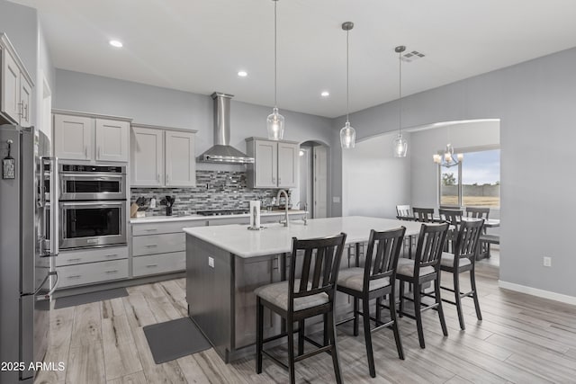 kitchen featuring visible vents, arched walkways, stainless steel appliances, decorative backsplash, and wall chimney exhaust hood